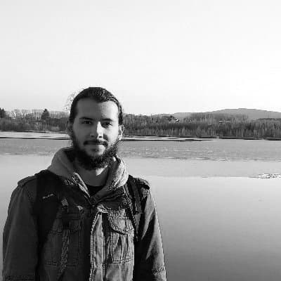 Young man with a backpack standing by a lake with trees and hills in the background, black and white photo